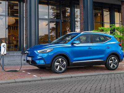 Ein blaues Elektroauto l&auml;dt an einer Ladestation vor einem modernen Geb&auml;ude, was Elektromobilit&auml;t im Jahr 2022 zeigt.